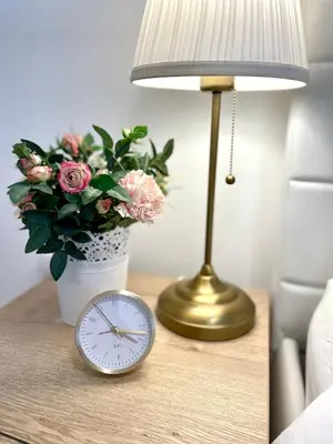 a table with a lamp and a clock and a vase of flowers at Tiara Vracar Apartment in Belgrade