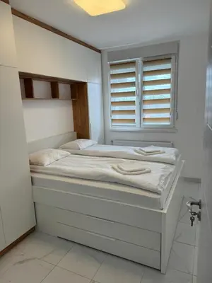 a white bedroom with two beds and a window at Apartman Biser 5 in Ruma