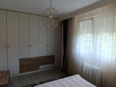 a bedroom with a chandelier and a bed and a window at Apartman Kokan in Obrenovac