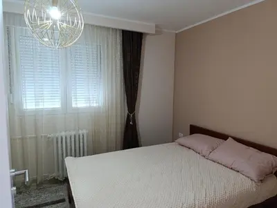 a bedroom with a bed and a chandelier and a window at Apartman Kokan in Obrenovac