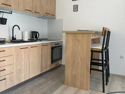 a kitchen with wooden cabinets and a table with a chair at Apartman Peric in Ruma