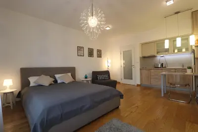 a bedroom with a bed and a kitchen and a chandelier at Savada Delta City - stan na dan Novi Beograd in Belgrade