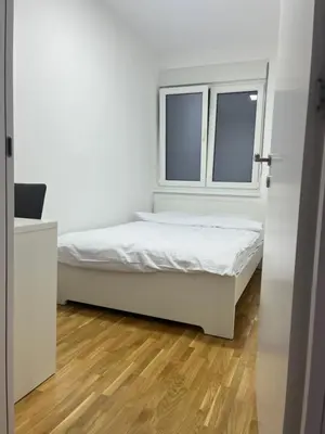 a white bedroom with a bed and a window at Apartman Katarina in Pančevo