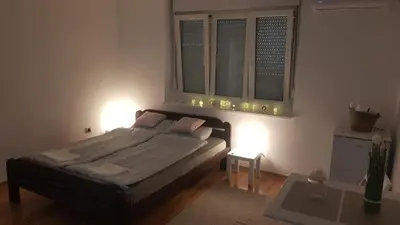 a bedroom with a bed and two windows and a table at Apartman Vojvoda 1 in Sajmište