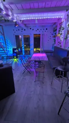 a room with chairs and tables and purple lights at Pool House 365 in Pe°ani