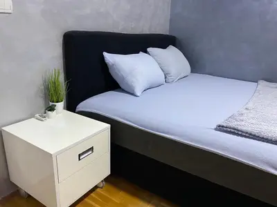 a bed with a white night stand next to a bed with a pillow at Crystal Apartman Obrenovac in Obrenovac