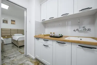 a kitchen with white cabinets and a sink and a bed at NAŠ Apartman in Voždovac