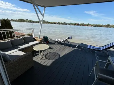 a boat deck with a couch and chairs on the water at Beautiful houseboat on the Sava river in Belgrade