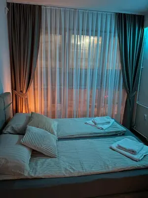 an unmade bed with a window with blue curtains at Lux Vracar by Magenta in Belgrade