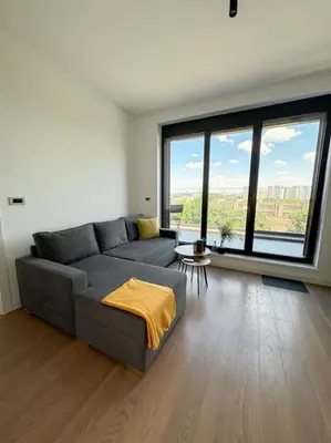 a living room with a gray couch and large windows at West 65 airport city apartment in Belgrade