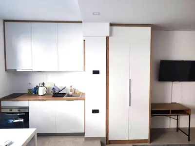a kitchen with white cabinets and a table and a tv at Asja studio in Belgrade