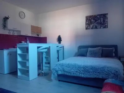 a bedroom with a blue bed and a table and a kitchen at AlejaPark Inđija in Železnicka Stanica Inđija Selo