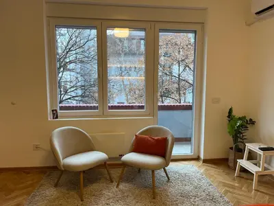 two chairs in a living room with two windows at Skadarlija Urban Nest in Belgrade