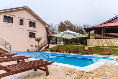 a house with a swimming pool with benches and an umbrella at Alrawda Resort in Risti°i
