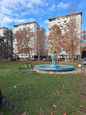 a fountain in a park with a bench and buildings at Royal apartment Novi Mercator in Belgrade