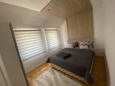 a small bedroom with a bed and two windows at Apartman LIMA in Belgrade