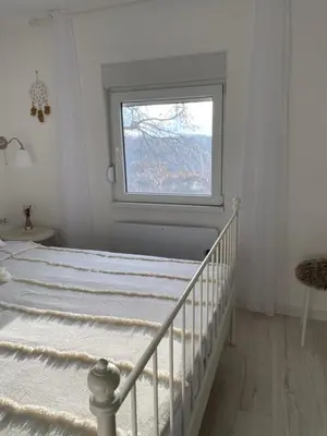 a white bedroom with a bed and a window at Vikendica Fruška lipa in Čortanovci