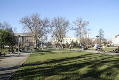 a park with people sitting on benches and trees at Yulia's beautiful studio in Belgrade