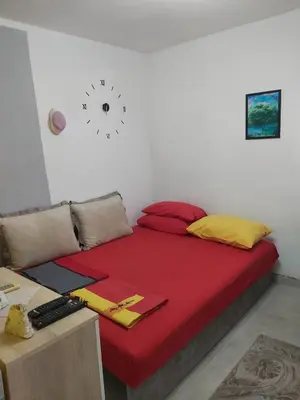 a bed with red and yellow pillows and a clock on the wall at Drago Sutomore 2025 in Borča