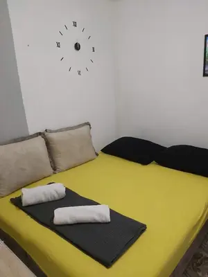 a yellow bed with two pillows and a clock on the wall at Drago Sutomore 2025 in Borča