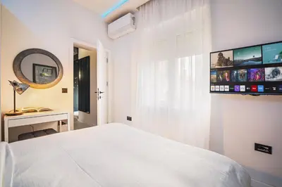 a white bedroom with a bed and a tv on the wall at Prime Location Modern Luxury in Bohemian Skadarlija! in Belgrade