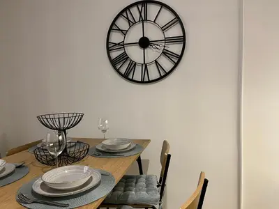 a dining room table with a clock on the wall at Liberte Apartments Voždovac in Belgrade
