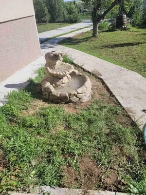 a stone bird bath in the grass next to a sidewalk at Vila Restart Čortanovci in Čortanovci