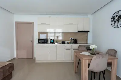 a kitchen with white cabinets and a table with chairs at Kolonja Apartmani in Arandjelovac