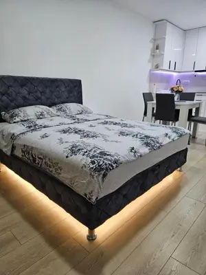 a bed in a room with a table and a kitchen at Miss LUX in Mladenovac