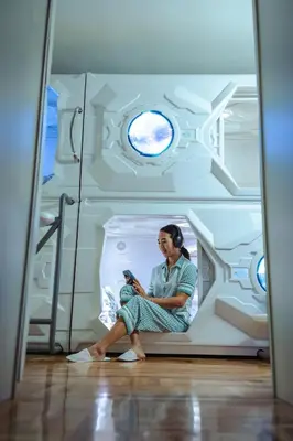 a woman sitting in a hospital room looking at a cell phone at Belgrade Beocean Capsule Hostel in Belgrade