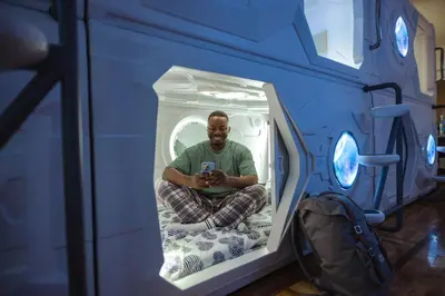 a man sitting on a bed in a blue room at Belgrade Beocean Capsule Hostel in Belgrade