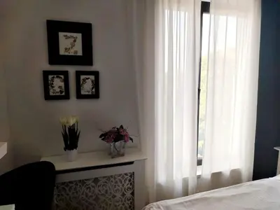 a bedroom with a window with white curtains and flowers at Benvenuti STAR in Belgrade