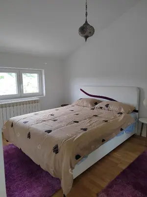 a bed in a white bedroom with a purple rug at Lux Apartman Banjica in Bukorovac
