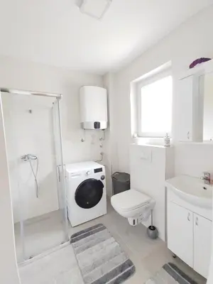 a white bathroom with a washing machine and a toilet at Lux Apartman Banjica in Bukorovac