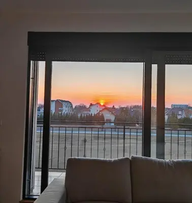 a couch in front of a window with a sunset at Airport sunset apartment in Ledine