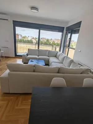 a living room with a large couch in a room with windows at Airport sunset apartment in Ledine