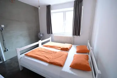 a bedroom with a bed with orange sheets and a window at Hostel Fair and Square in Belgrade
