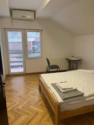 a bedroom with a bed and a chair and two windows at Aliyah Hostel in Belgrade