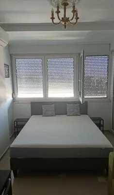 a bedroom with a bed with two windows and a chandelier at Ogi apartment Beograd in Belgrade