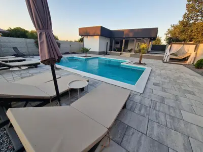 a swimming pool with an umbrella and tables and chairs at Elin House in Inđija