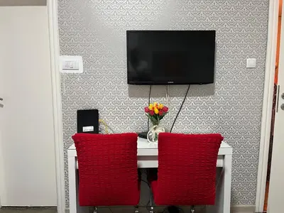 a table with two red chairs and a tv on a wall at Bridge studio in Belgrade