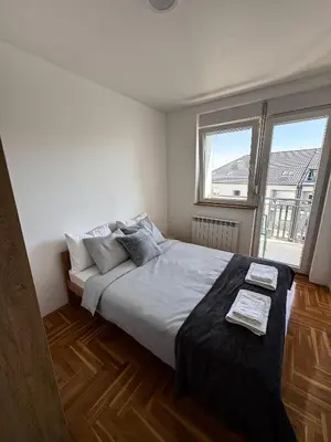a bedroom with a large bed and two windows at Limpio Apartman 2 in Belgrade