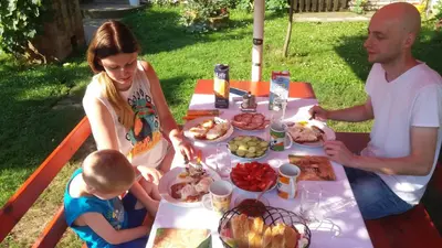 a family sitting at a picnic table eating food at Santa Maria Apartment in Donji Kovilj