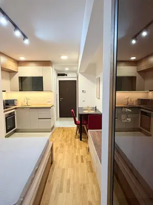 a kitchen with white cabinets and a table with a red chair at Apartment UNA in Pančevo