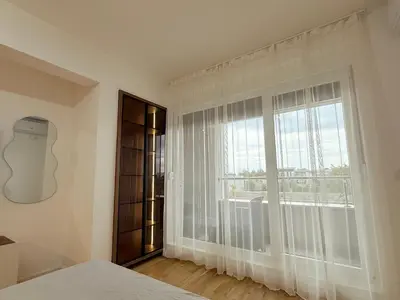 a bedroom with a large window with white curtains at Apartment UNA in Pančevo