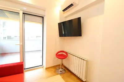 a red chair in a room with a tv on the wall at Grandeur Slavija in Belgrade