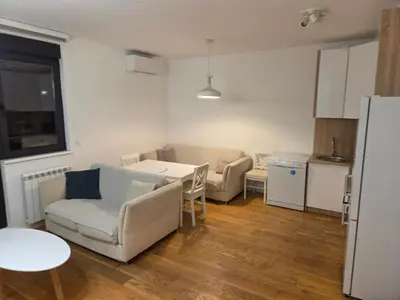 a living room with a table and chairs and a kitchen at Apartman-Stan in Belgrade