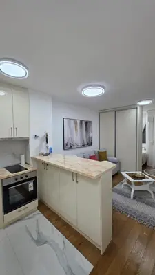 a kitchen with white cabinets and a living room at Apartman Beograd in Belgrade