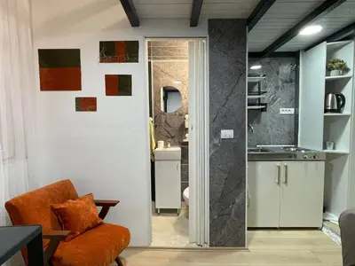 a living room with an orange chair and a kitchen at Princip Apartman in Belgrade