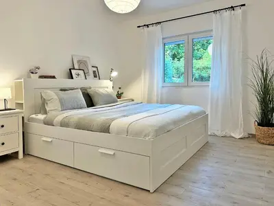 a white bedroom with a large bed and a window at Mali Raj in Mala Ivanča